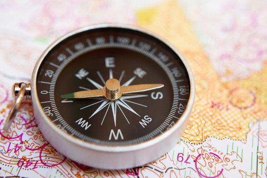Round compass on colorful topographic map for orienteering or rogaining sport, close up view at shallow depth of field. Travel, recreation and active lifestyle concept.