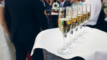 Elegant dressed waiter holding tray with champagne in glasses at wedding reception in luxury restaurant, catering concept