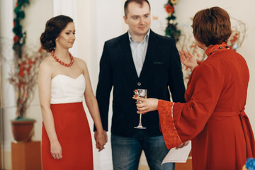 Mother in law pronouncing toast to happy newlywed couple, woman with champagne glass drinking to bride and groom at wedding ceremony in registry office