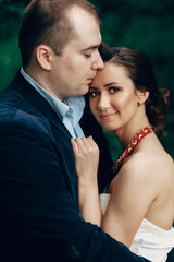 Portrait of happy newlywed couple, happy handsome groom and beautiful bride in elegant dress hugging outdoors in a park, honeymoon walk in a garden