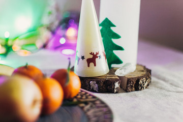christmas rustic table with candle with reindeers and felt tree and fruits on colorful lights background. space for text. seasonal holidays card concept