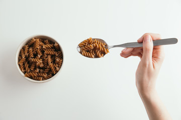 Whole grain fusilli pasta in spoon, white background, selective focus