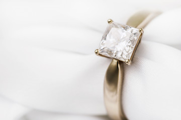 Gold wedding ring with a large diamond on a silk fabric with copy space, close-up