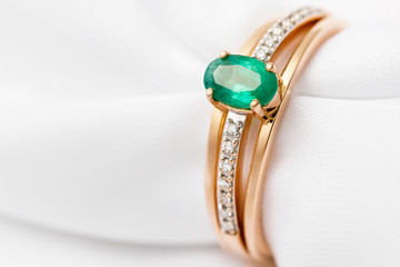 Beautiful golden ring with emerald and cubic zirconias on white silk with copy space