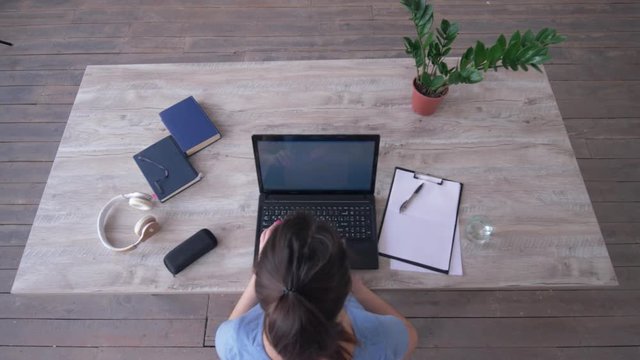 student girl uses laptop while typing text on keyboard and writes notes in clipboard sitting at the desk during e-learning, top view