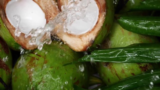 Fresh young coconut split in half showing white flesh with pile of coconuts