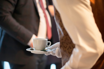Waiter's hands with a cup on the background of a man