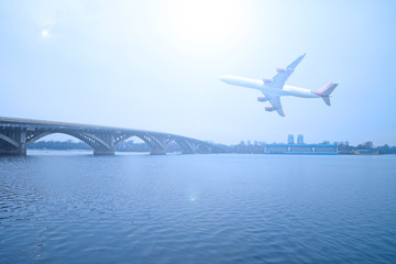 Naklejka premium The plane over the river and the bridge in the city. Cloudy day.