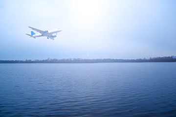 Fototapeta na wymiar Airliner over the river in a cloudy dark sky. The sun shines brightly.