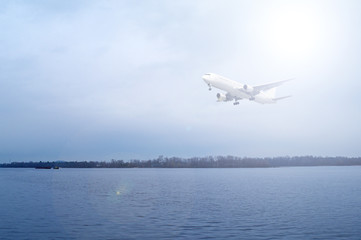 Fototapeta na wymiar Airliner over the river in a cloudy dark sky. The sun shines brightly.