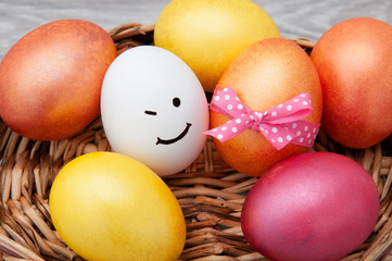 Easter eggs with a smile on a wooden basket on a gray background. Congratulatory card with Easter.