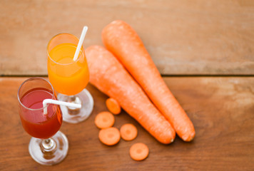 Carrot juice glass and fresh carrot on wooden background on summer day - selective focus