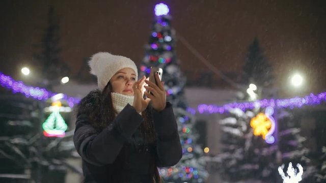 a woman with a smartphone on the square near the Christmas tree, shares photos on social networks