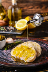 Pouring of tasty olive oil from bottle onto fresh bread