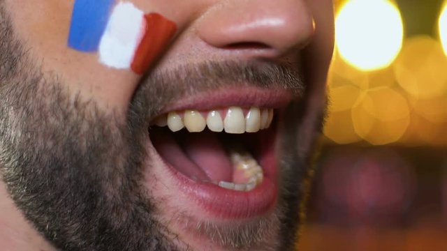 Man fan with painted French flag on cheek emotionally cheering for national team