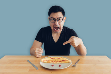 Angry and mad face of man is eating homemade breakfast set of omelet.