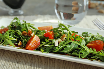 Plate with tasty arugula salad on table