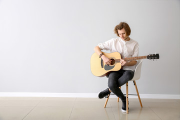 Handsome young man playing guitar near light wall