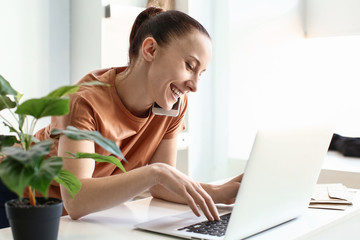 Woman talking by phone while working on laptop indoors