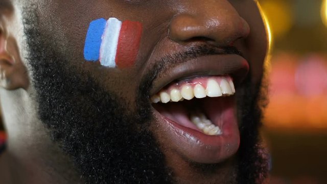 Black male fan with French flag on cheek cheering for national team victory