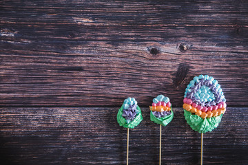 Colorful sweet homemade meringues in the form of eggs on wooden background. Many sweet zephyrs. Trendy top view dessert image.