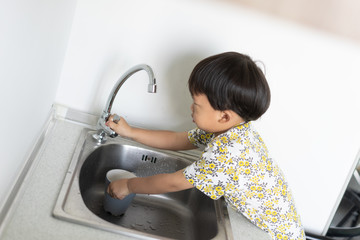 The boy is helping the mother to do the housework by washing a glass and a dish.