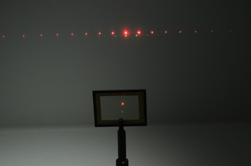 In a darkened room, two laser beams from a source under the camera, hits an optical grid and an interference pattern apppears on the wall in the background. This grid has 100 lines per millimeter.