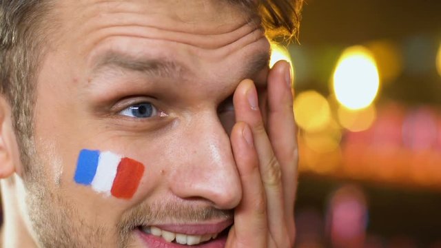 Male fan with French flag on cheek upset about favorite sports team losing game
