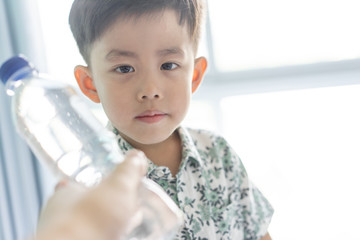 The boy is giving a bottle of water from fridge to his mom.