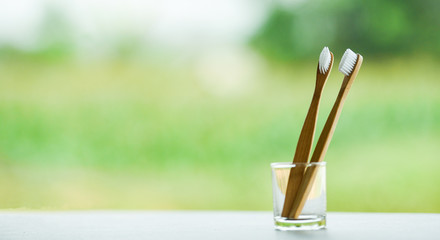 Zero waste Bathroom use less plastic concept / bamboo toothbrush in glass on nature green background
