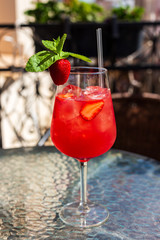 A refreshing red drink with ice, strawberry and mint in a wine glass on a city cafe terrace