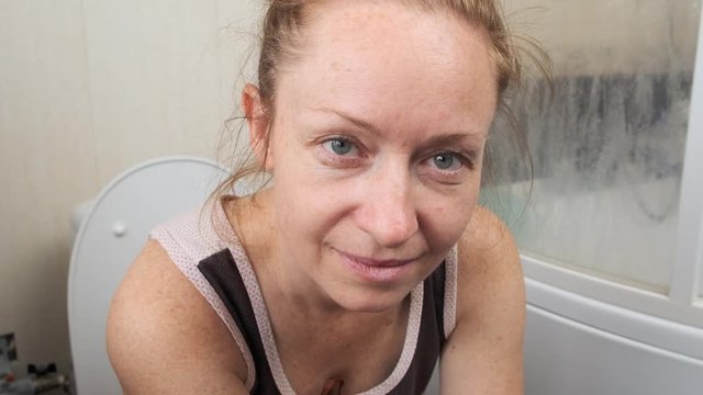 Adult woman sitting on the toilet and straining in the bathroom.