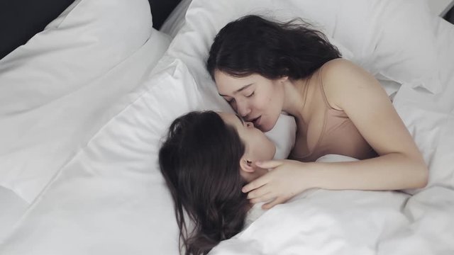 Lesbian couple hugging and smiling while lying together in bed at home. Young lesbians kisses and hugs after wake up
