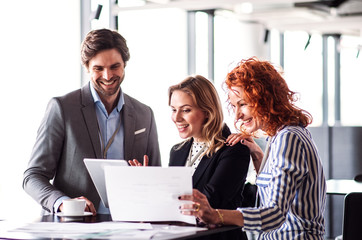 A group of young business people with tablet sitting in an office, talking.