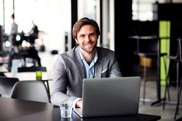 A portrait of young businessman with computer in an office, looking at camera.