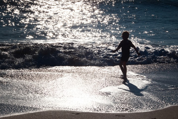 Silhouette of a little boy playing on beach with water.
