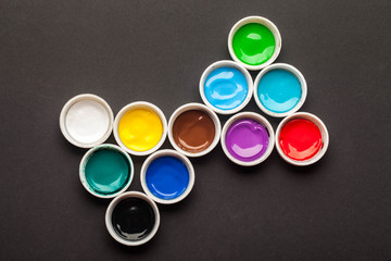 Jars with different colors of acrylic paint on a black background