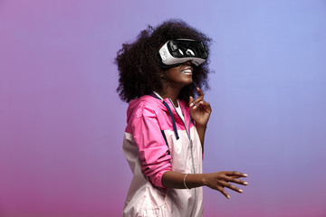 Mod young brown-haired curly girl dressed in the pink sports jacket uses the virtual reality...