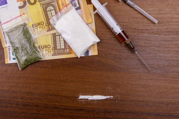 Different type of drugs: cocaine, heroin syringe and dried cannabis and euros on a table. Drug use, drug trafficking, crime and addiction concept