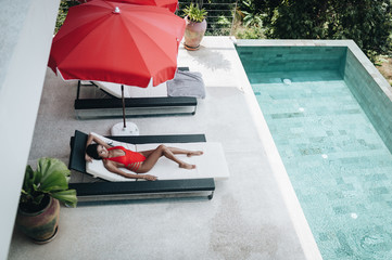 Sexy asian woman in a red swimsuit laying in sunbed at the poolside