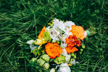 Beautiful wedding bouquet is lying in the grass. Engagement rings are on the flowers. Orange colours of fall and autumn in floral composition.
