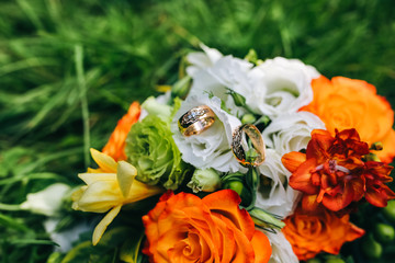 Beautiful wedding bouquet is lying in the grass. Engagement rings are on the flowers. Orange colours of fall and autumn in floral composition.