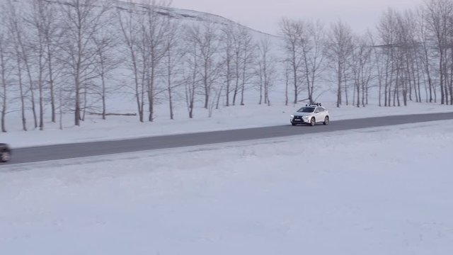 One white crossover wagon car with roof rack alone driving on highway through flat snowy field at winter evening sky - Aerial drone footage
