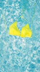 Yellow bikini in clean blue water of the pool. Instagram mobile story or stories size. Mobile wallpaper