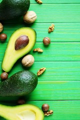 Avocado cut in half lies on a green wooden background surrounded by nuts and green salad leaves, snack for Keto diet