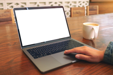 Fototapeta premium Mockup image of a woman's hand using and touching on laptop touchpad with blank white desktop screen with coffee cup on wooden table