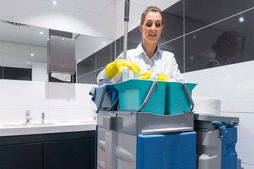Janitor or charlady with her work tools looking at camera in toilet