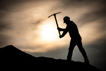 Concept Labor Day: Labor man standing holding a pickaxe with a warm sunset light