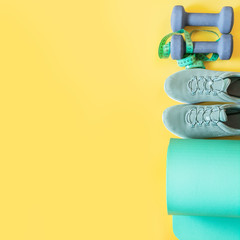 Sport and fitness equipment, dumbbells, fitness shoes, measuring tape, yoga mat on yellow. Space for text.