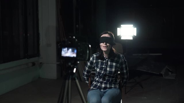 Related young woman hostage with a blindfold sitting in front of a camera lens